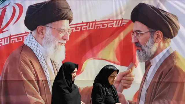 سيدتان تسيران وخلفهما صورة للمرشد الأعلى الإيراني الراحل آية الله علي خامنئي وابنه مجتبى.