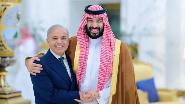 شهباز شریف با کت آبی در حال بغل کردن محمد بن سلمان با عبای قهوه‌ای و با چفیه قرمز و عقار سیاه