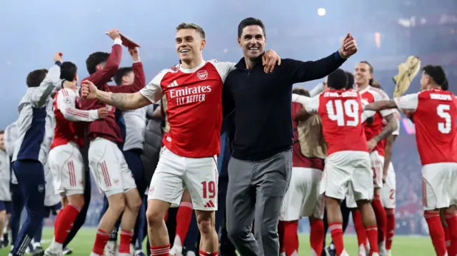 Ikipe ya Arsenal yishimiye intsinzi yayo, ifoto igaragaza umutoza ari kumwe n’umwe mu bakinnyi bafatanye ku rutugu abandi na bo bari inyuma yabo bishimye.