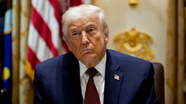 Perezida Donald Trump, yambaye ikoti yirabura, ishati igomba kwera n'ikaruvati ituruka irimwo utubara twirabura, ariko araba muri camera