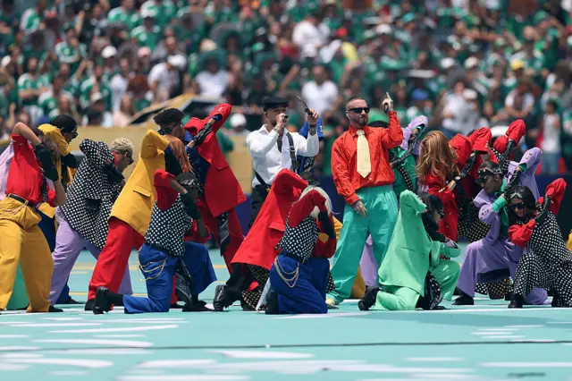 J Balvin con Ryan Castro rodeados de bailarines y color.
