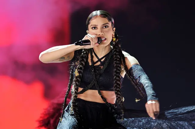 Anita durante um show. Ela usa tranças, uma roupa preta e está com o microfone na mão