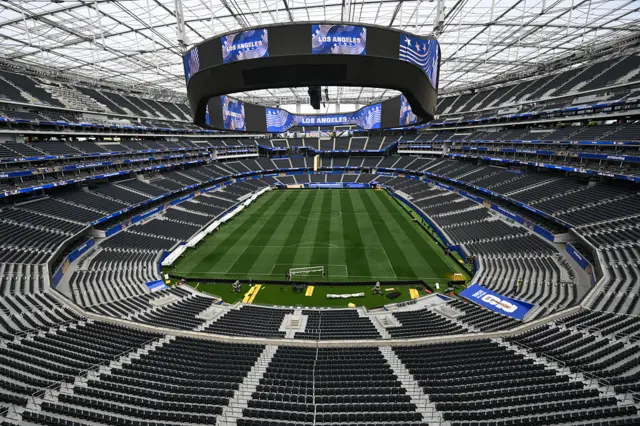 Imagem aérea de um estádio grande, vazio, com uma tela no meio