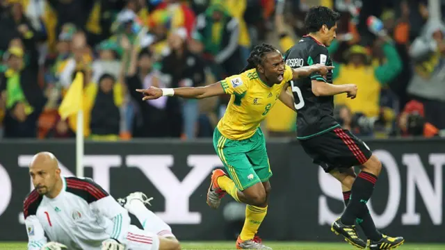 يحتفل سيفيو تشابالالا، لاعب منتخب جنوب أفريقيا، بتسجيله الهدف الافتتاحي، بينما يبدو ريكاردو أوسوريو (يمين) وحارس المرمى أوسكار بيريز، لاعبا منتخب المكسيك، محبطين خلال بطولة كأس العالم لكرة القدم 2010 في جنوب أفريقيا.