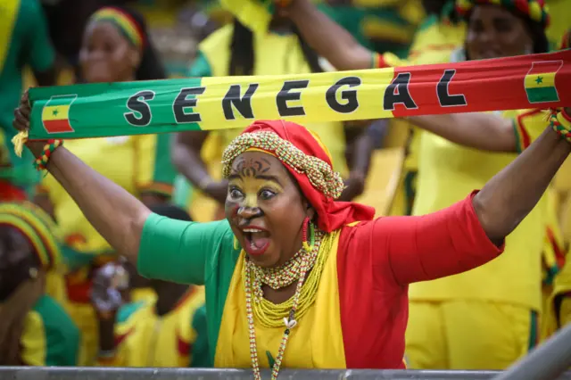 Une supportrice de l'équipe nationale du Sénégal tenant une écharpe sur laquelle est écrite "SENNEGAL".