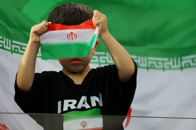 کودک خردسالی در حال کلنجار رفتن با پرچم ایران روی سکوها