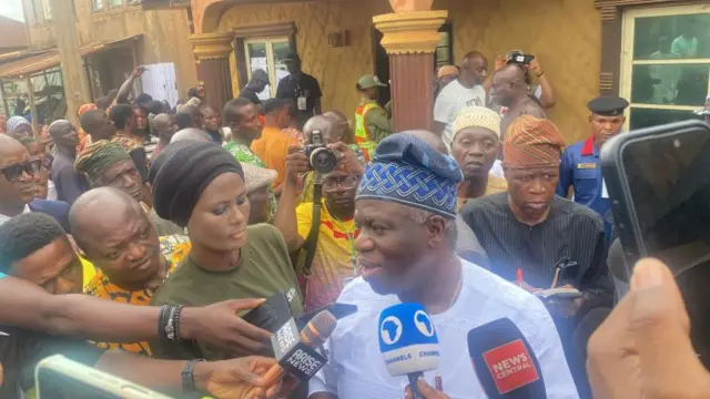 Oluwole Oyedele wọ aṣọ funfun, awọn gbohungbohun wa niwaju rẹ, ọpọ ero wa lẹyin rẹ