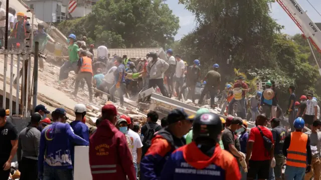 Decenas de miembros de los servicios de emergencia, algunos de ellos con cascos y mascarillas, registran los escombros de un edificio derrumbado.