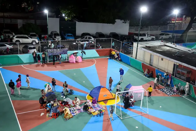 Personas en tiendas de campaña en una pista deportiva en Caracas.