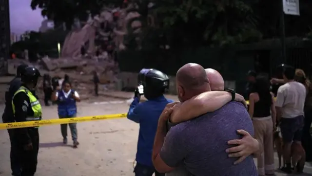 Dos personas de abrazan conmovidas frente a un edificio caído en Caracas.