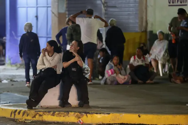 Un grupo de personas sentadas en la acera en medio de la noche en Caracas.