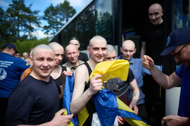 Мужчины с бритыми головами держат в руках украинские флаги, стоя на выходе из автобуса.