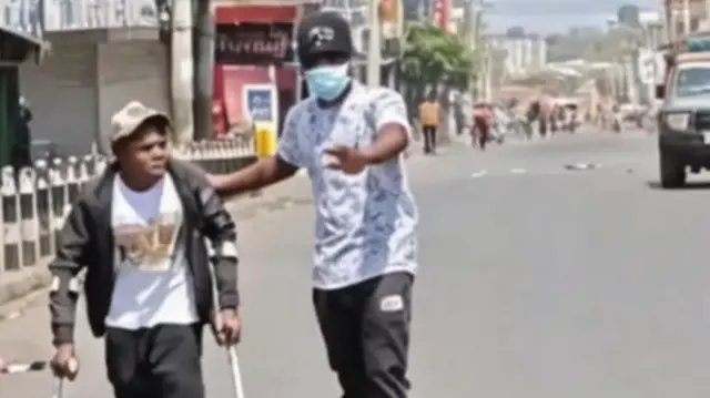 Mwanamume akimsaidia mtu anayeishi na ulemavu kuvuka barabara kabla ya kukamatwa na maafisa wa polisi wakati wa maandamano ya Alhamisi