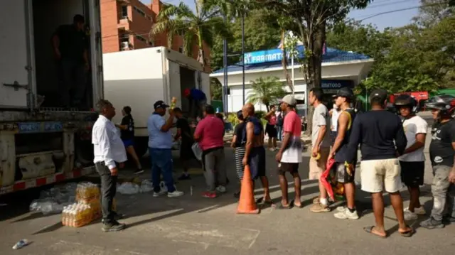 Fila de personas detrás de camiones que reparten ayuda