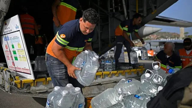 Trabajadores cargan garrafones de agua desde un avión, apilándolos en una rampa junto a más suministros.