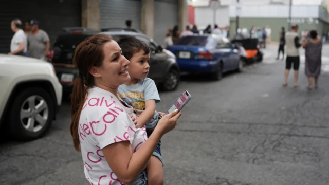 Una mujer sostiene un teléfono y un niño mientras su rostro refleja una expresión de angustia.