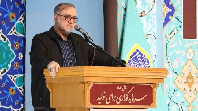محمد اکبرزاده با کاپشن سیاه پشت تریبون چوبی