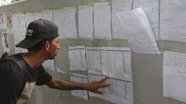 un hombre lee unas listas de nombres pegadas a una pared