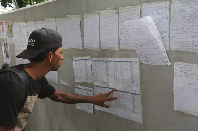 Un hombre mira una lista en busca de los nombres de familiares desaparecidos.