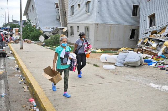 Dos mujeres llevando cajas pasan por delante de edificios derrumbados