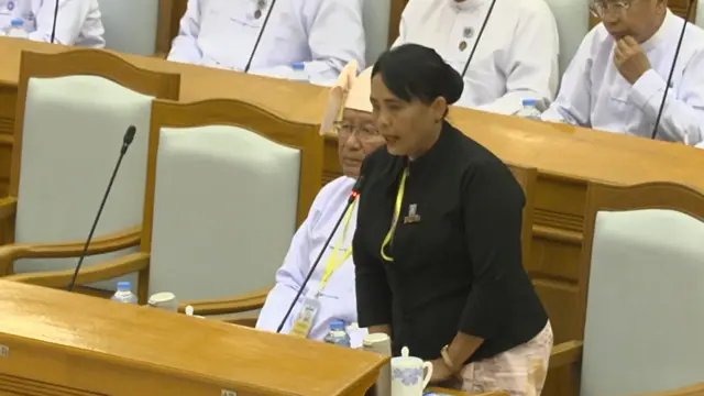 လွှတ်တော်မှာ ရှေ့နေ့ ဝတ်စုံအမဲရောင်ဝတ်ပြီး မတ်တပ်ရပ်စကားပြောနေတဲ့ ဒေါက်တာသီတာဦး