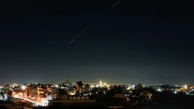 Umurongo w'igisasu mu kirere ca Israel mw'ijoro, hejuru y'inyubakwa nyinshi ziriko amatara