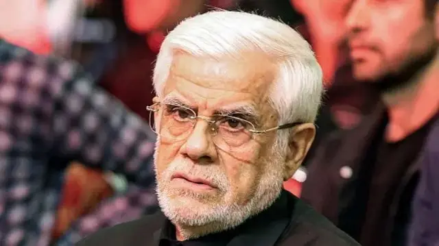 النائب الأول للرئيس الإيراني، محمد رضا عارف يبدو أنه جالس بين حضور ويرتدي بدلة رسمية سوداء مع قميص أسود دون ربطة عنق، بشرته حنطية وشعره رأسه ولحيته أبيض ويرتدي نظارات طبية.