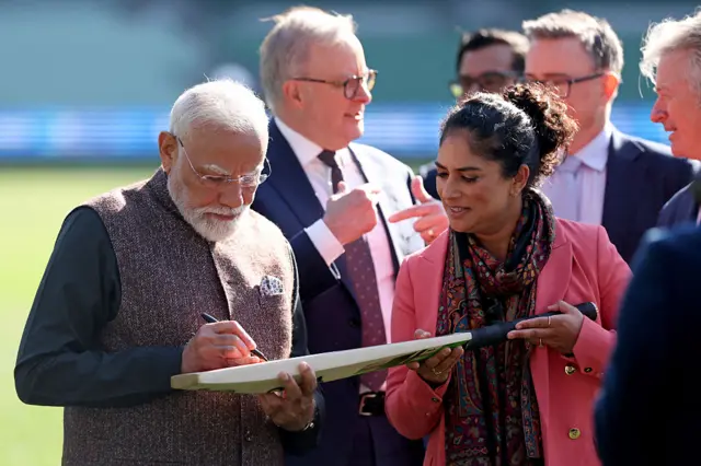 मेलबर्न क्रिकेट ग्राउंड में एक क्रिकेट बैट पर हस्ताक्षर करते पीएम मोदी