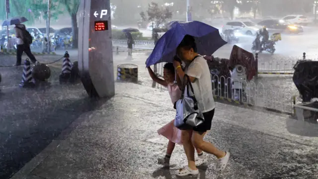 大雨下北京某停車場外一位老太與一名女孩撐著小雨傘小跑前往避雨(中新社圖片10/7/2026)
