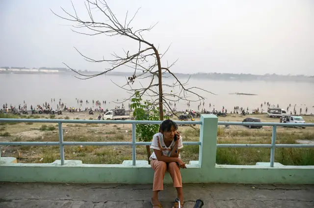 ကမ်းနားဘေးက အုတ်ခုံပေါ်မှာ အမျိုးသမီးတဦးထိုင်ပြီး ဖုန်းပြောနေတဲ့မြင်ကွင်း (ပုံဟောင်း)