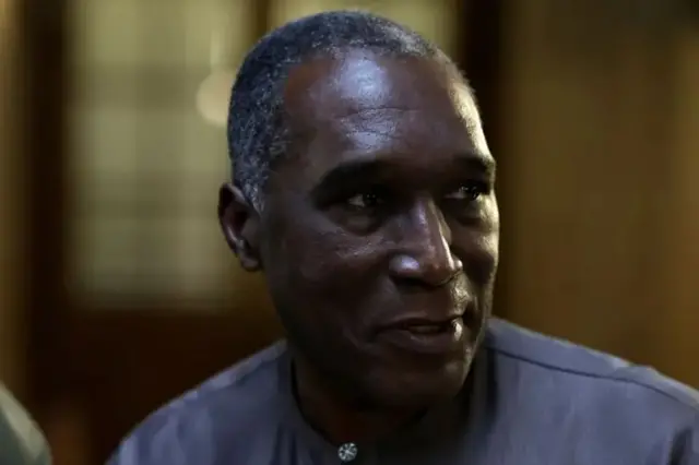 Dr Eugène Rwamucyo yambaye ishati y'ubururu arimo kuvuga araba ku ruhande. Ifoto yafashwe ku mugoroba.