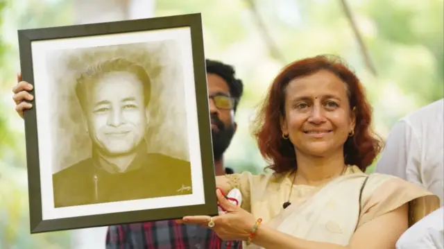 सोनम वांगचुक की तस्वीर लिए उनकी पत्नी गीतांजलि