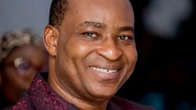 Umugabo urimo kumwenyura wambaye ishati y'iroza