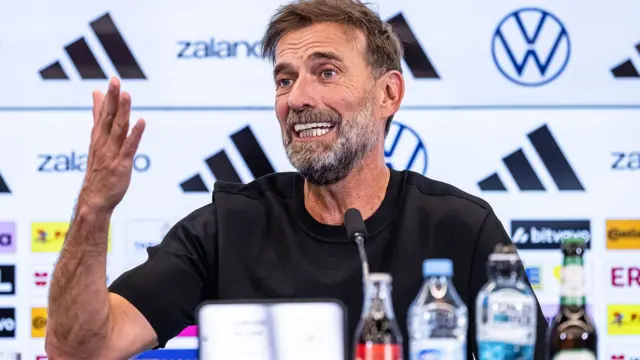 Jurgen Klopp akoze ikimenyetso n’ikiganza, mu kiganiro n’abanyamakuru ku itariki ya 24 Nyakanga (7) mu 2026. Yambaye umupira w’umukara w’amaboko magufi, arimo kuvugira mu ndangururamajwi, imbere ye hari ibyo kunywa byoroheje biri mu macupa, birimo n’amazi.