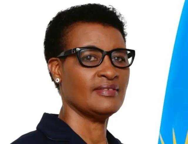 Donatille  Mukabalisa yambaye ishati y'umukara n'indorerwamo. Arareba muri 'camera'. Iruhande rwe hari ibendera ry'u Rwanda.