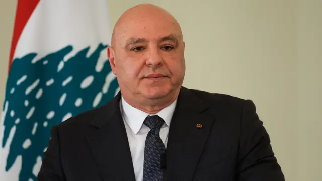 جوزف عون با کت و کراوات سیاه نشسته جلوی پرچم لبنان