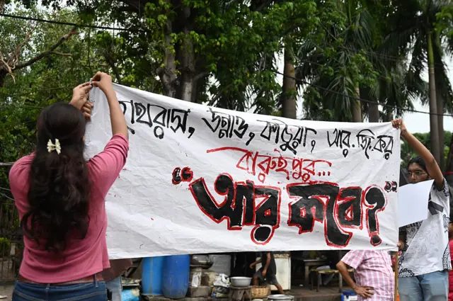 বারুইপুরে কিশোরীকে ধর্ষণ ও খুনের ঘটনায় প্রতিবাদের বার্তা লেখা একটি ব্যানার টানাচ্ছেন একজন নারী এবং একজন পুরুষ