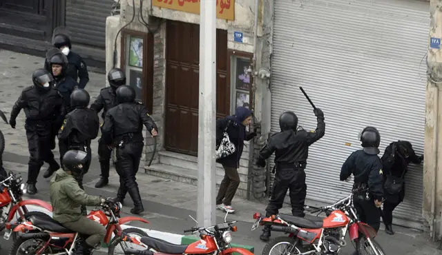رجال من الشرطة بملابس سوداء أحدهم يرفع عصا في وجه شخص مدني