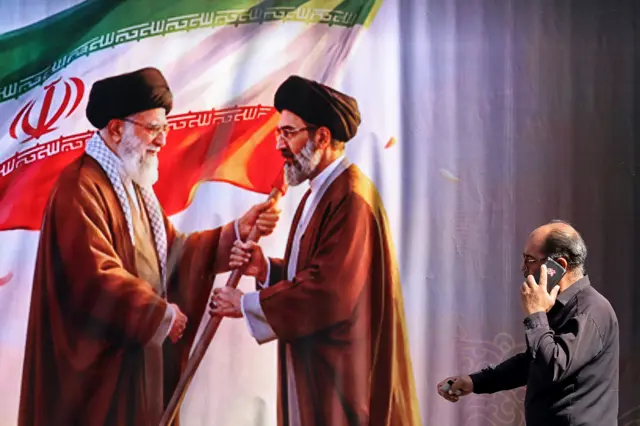 رجل يمر أمام لوحة في أحد شوارع طهران تظهر علي خامنئي ونجله مجتبى.