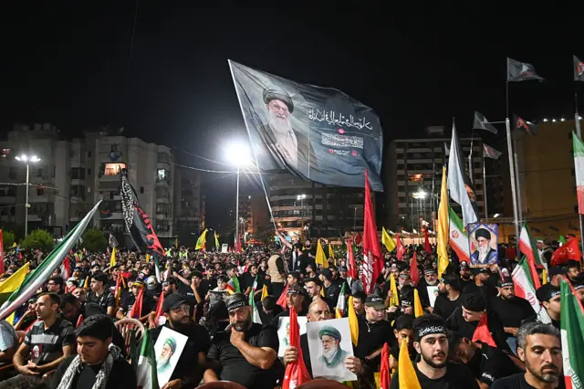 مئات الشبان باللباس الأسود ورايات حزب الله يجلسون وفي المقدمة بعضهم يرفع صور علي خامنئي
