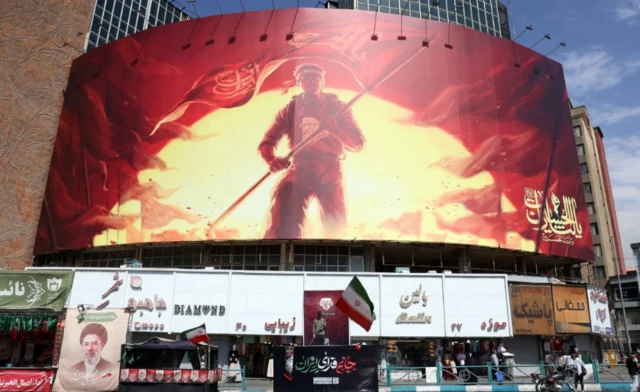 An Iranian man holds Iran's flag in front of a billboard at Valiasr Square