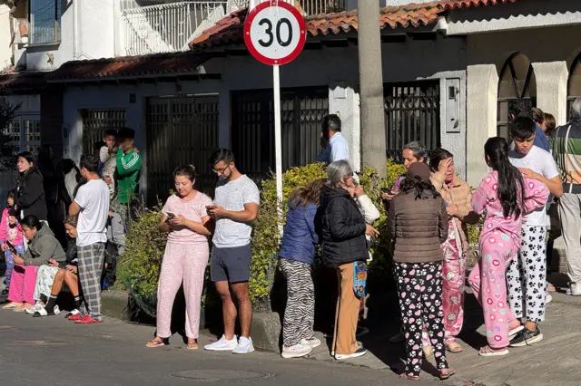 Personas en la calle en sus pijamas, algunos mirando sus teléfonos