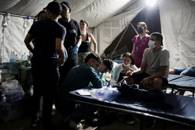 Equipo médico atiende a un rescatista de noche dentro de una tienda de campaña.