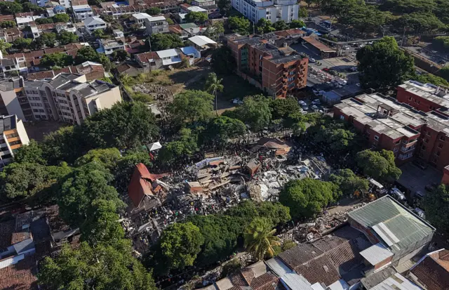Vista aérea de Cali, donde se ven numeros edigicios destrozados, muchos árboles y otros edificios en pie.