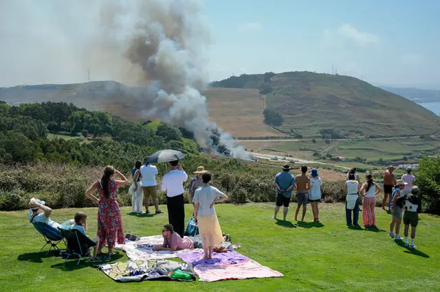 Varias personas esperan el eclipse mientras se produce un incendio forestal cerca en La Coruña