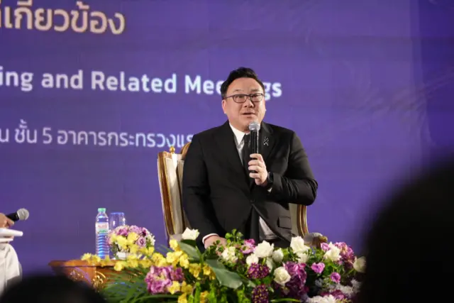 စင်ပေါ်မှာ အနောက်တိုင်းဝတ်စုံ အနက်ရောင်ဝတ်ပြီး ကုလားထိုင်မှာ ထိုင်ကာ မိုက်ခရိုဖုန်းကိုင်ပြီး စကားပြောနေတဲ့ ထိုင်းအလုပ်သမား ဝန်ကြီး ဂျူလာပွန် အမွန်ဝီဝပ်