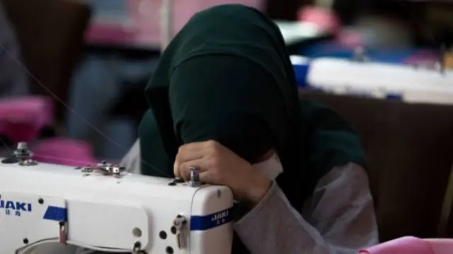 تصویر یک زن خیاط که به روی چرخ خیاطی اش سرش را گذاشته است.