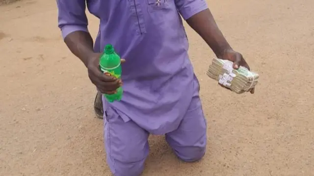 Di man wear purple cloth, e kneel down for ground and e hold money(cash) and and green bottle for hand
