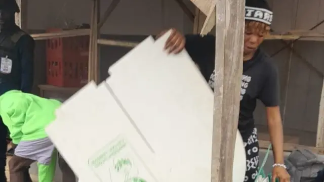 Woman wey dey hold di collapsed voting boot be like say dey dey put am back inside bag