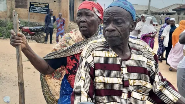 Elderly man and woman dey ontop okada, di man dey ride di okada whuile di woman sidon for back as she hold her stick